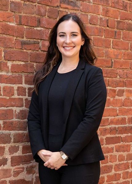 A woman in a black suit is standing in front of a brick wall.
