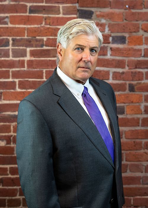 A man in a suit and tie is standing in front of a brick wall.