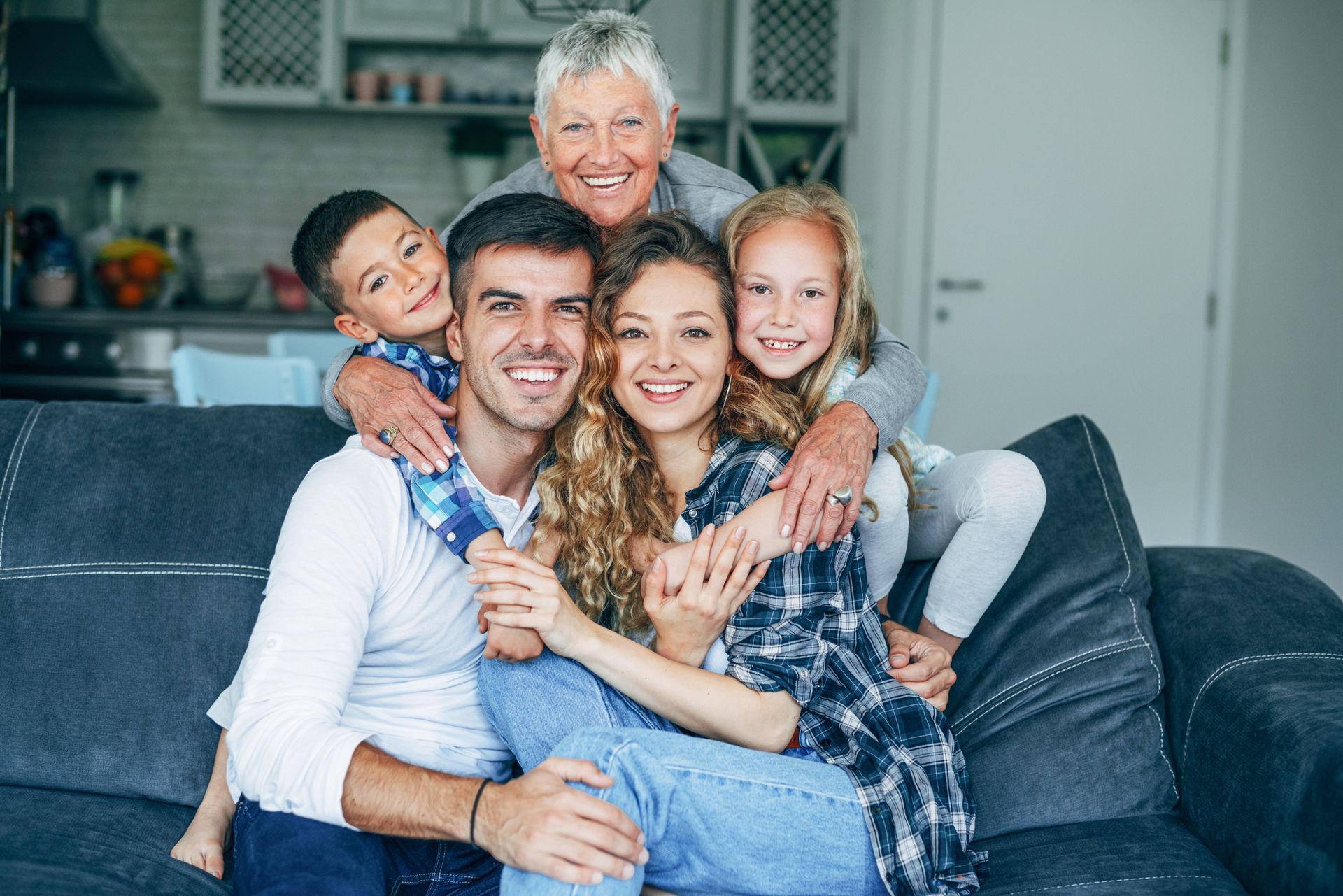 Family of five, including a grandmother, smiles on a couch.