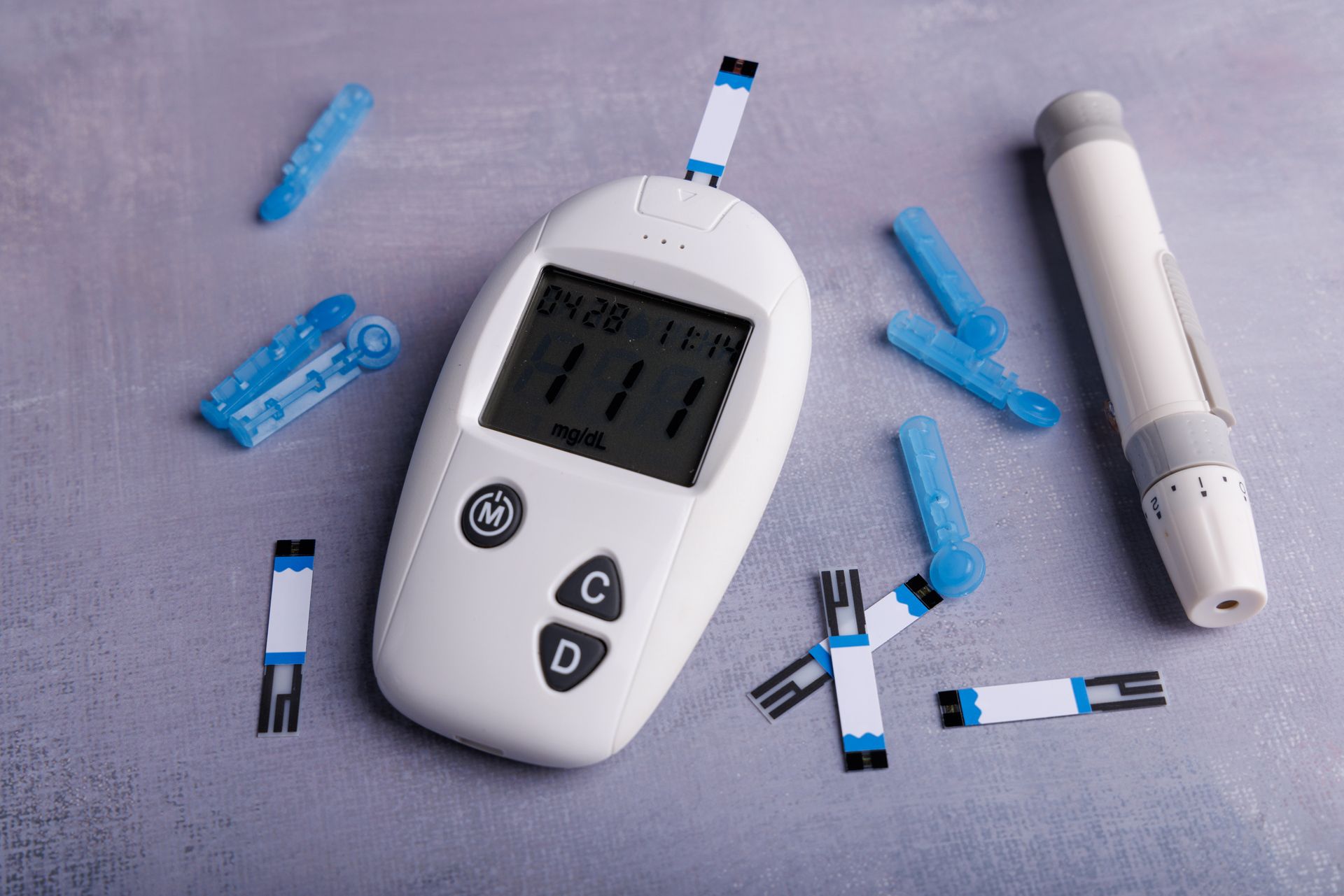 Blood glucose meter with test strips and a lancet on a gray surface.