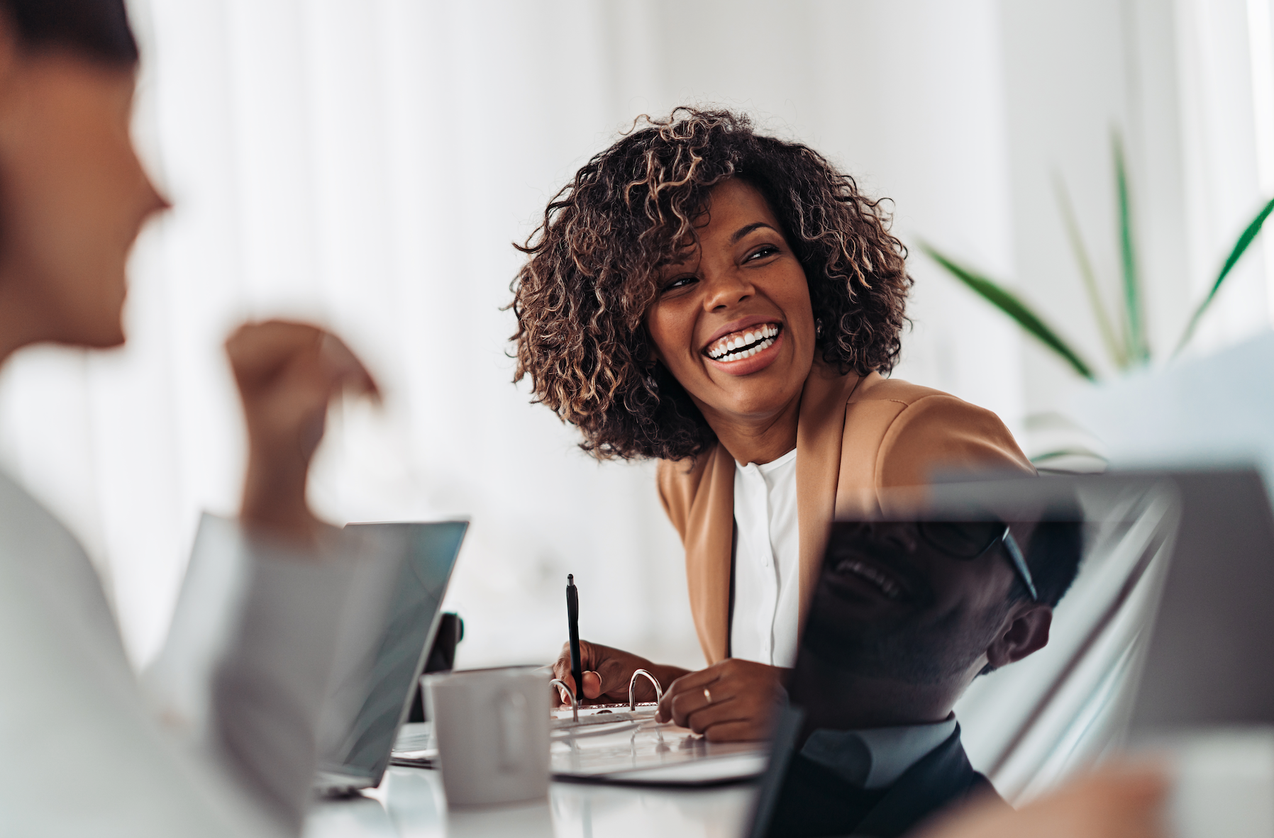 A woman is smiling while sitting at a table with other people.
