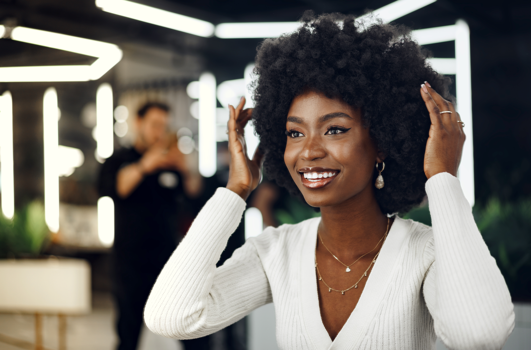 A woman with an afro is smiling and touching her hair.