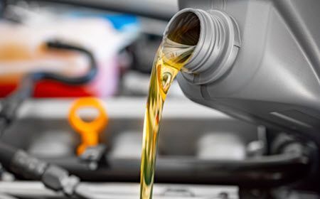 A bottle of oil is being poured into a car engine.  | Southwest Auto