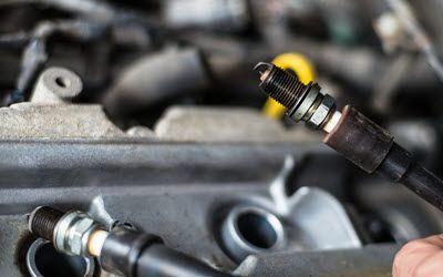 A person is holding a spark plug in front of a car engine.  | Southwest Auto