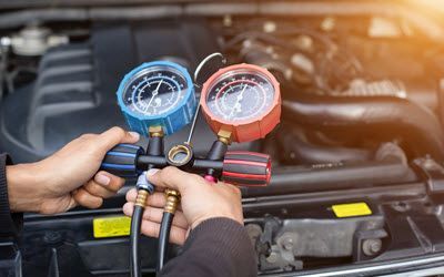 A man is holding two gauges in front of a car engine.  | Southwest Auto