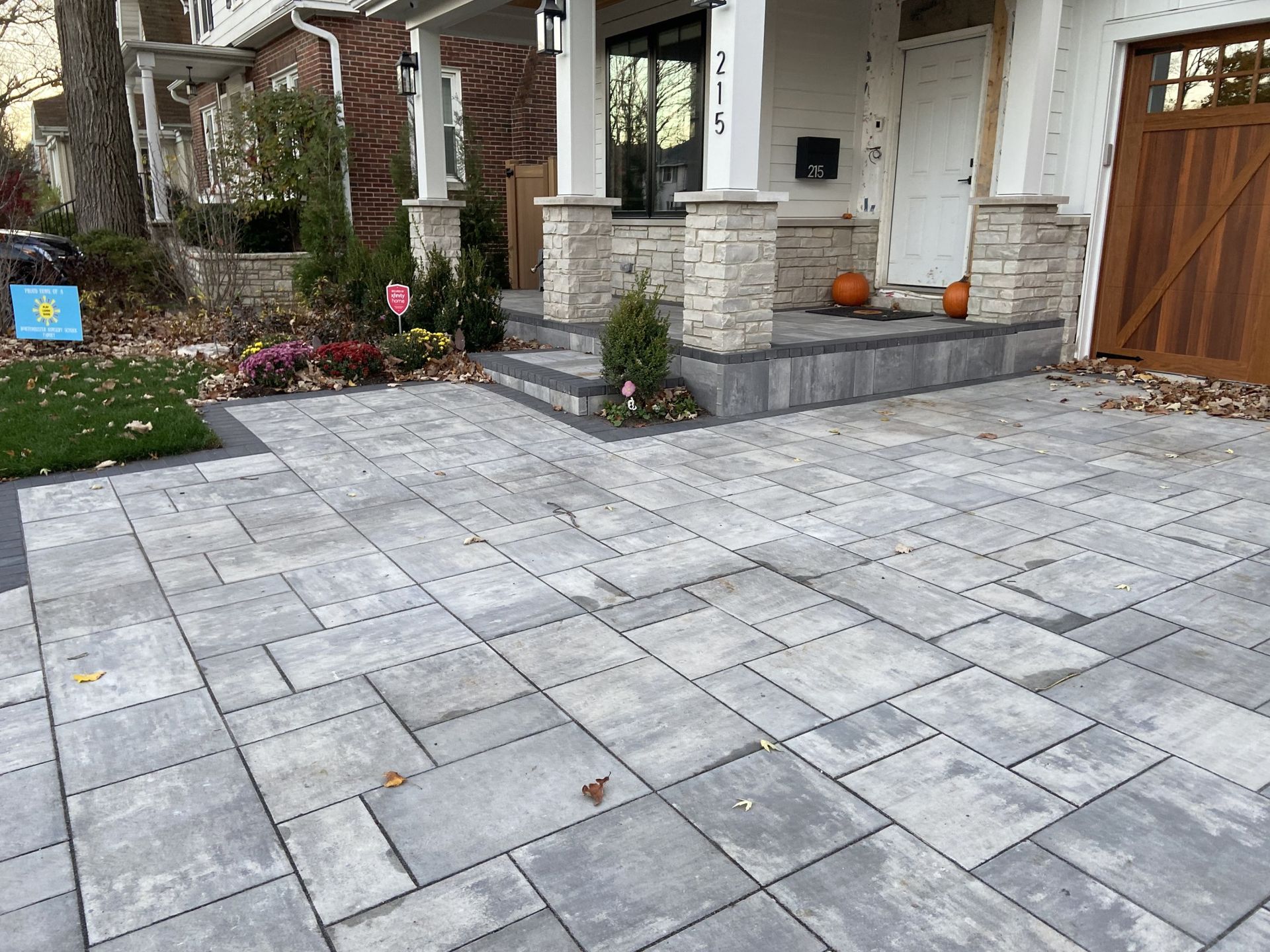 Gray pavers leading to a house with stone columns, porch, and a wooden garage door.