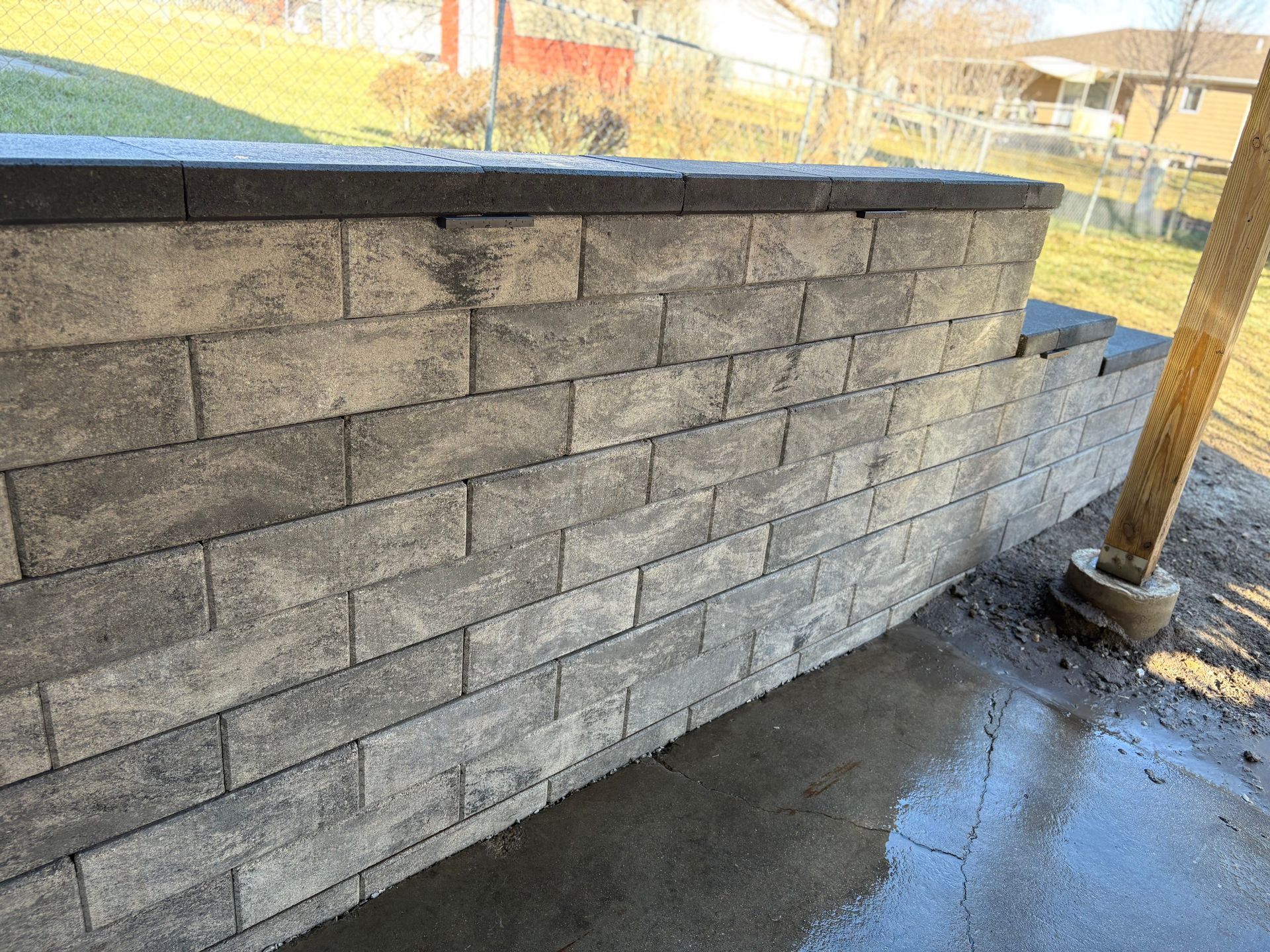Gray brick retaining wall with dark top and wet concrete patio.