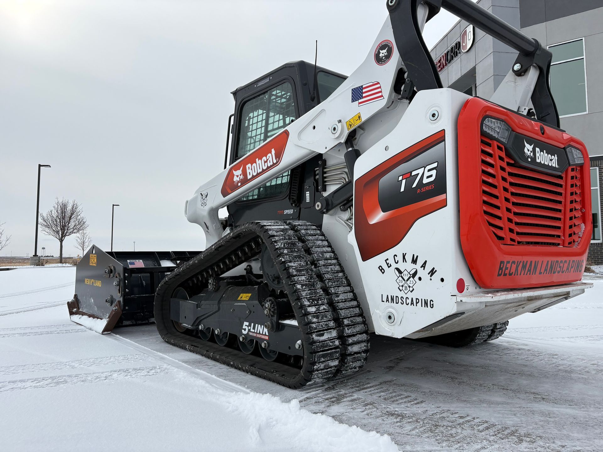 Bobcat T76 track loader with snowplow clearing snow. White and red loader on a snowy surface.