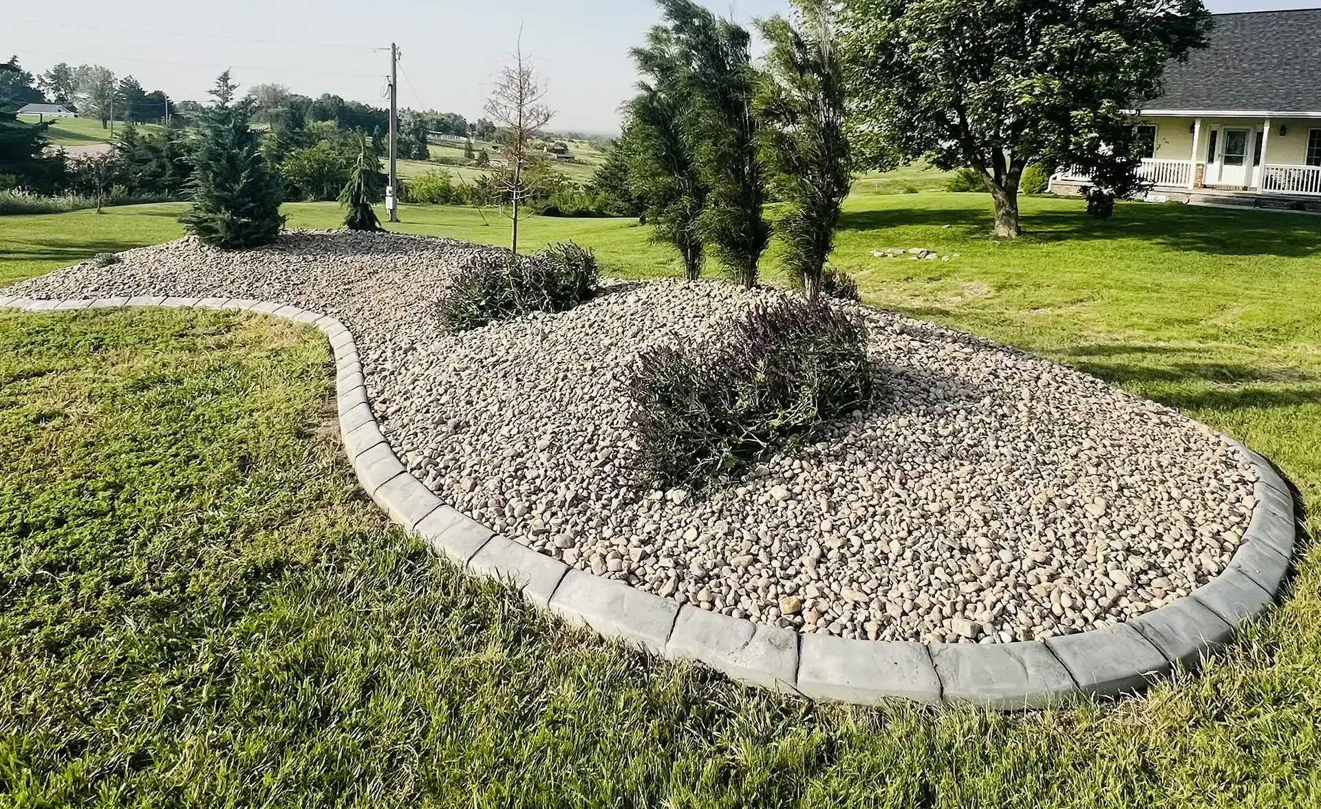 Stone-covered garden bed with border and plants in a grassy yard.