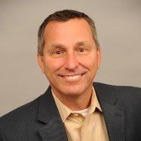 A man in a suit and tan shirt is smiling for the camera.