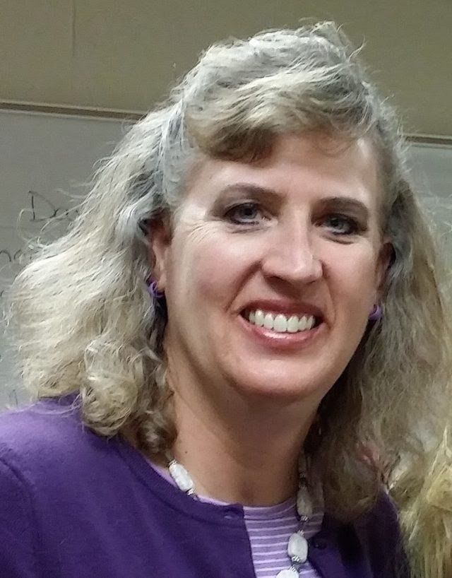 A woman in a purple jacket and striped shirt is smiling for the camera.
