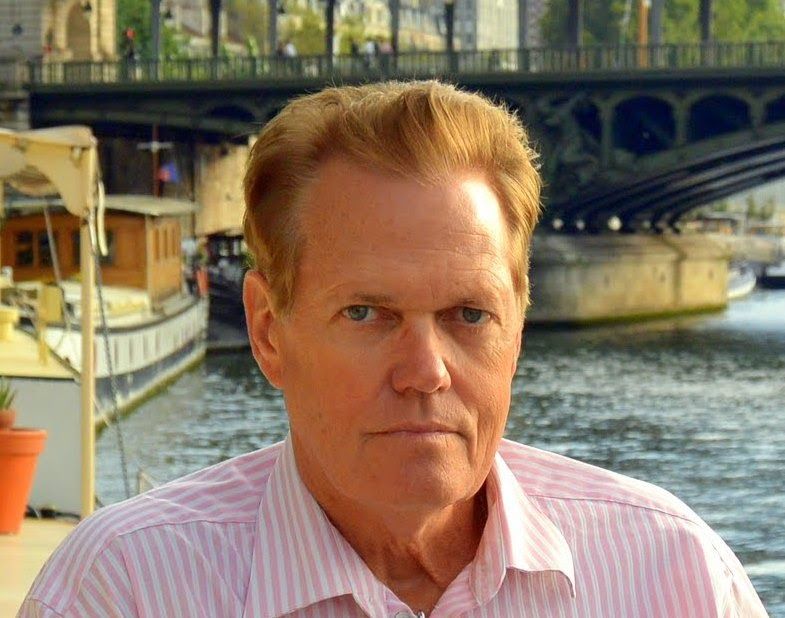 A man in a pink striped shirt is standing in front of a body of water.