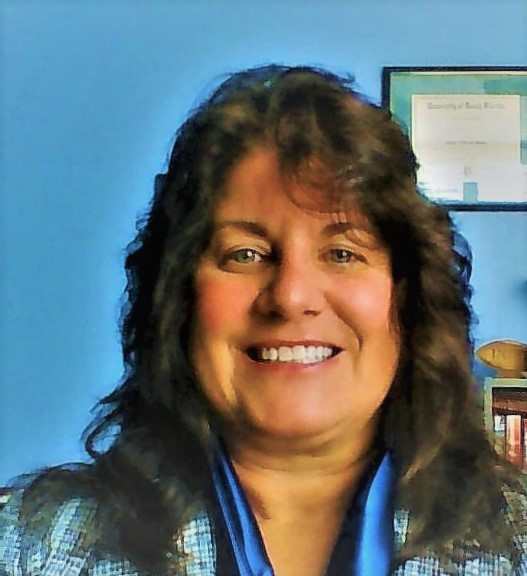 A woman with long hair is smiling in front of a blue wall