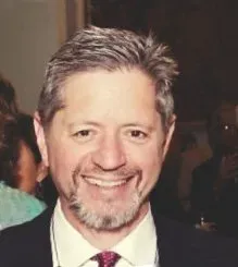 A man with a beard is wearing a suit and tie and smiling.