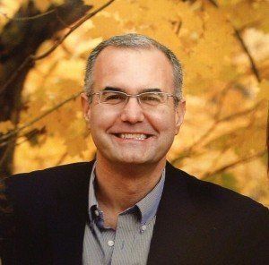 A man wearing glasses and a suit is smiling for the camera