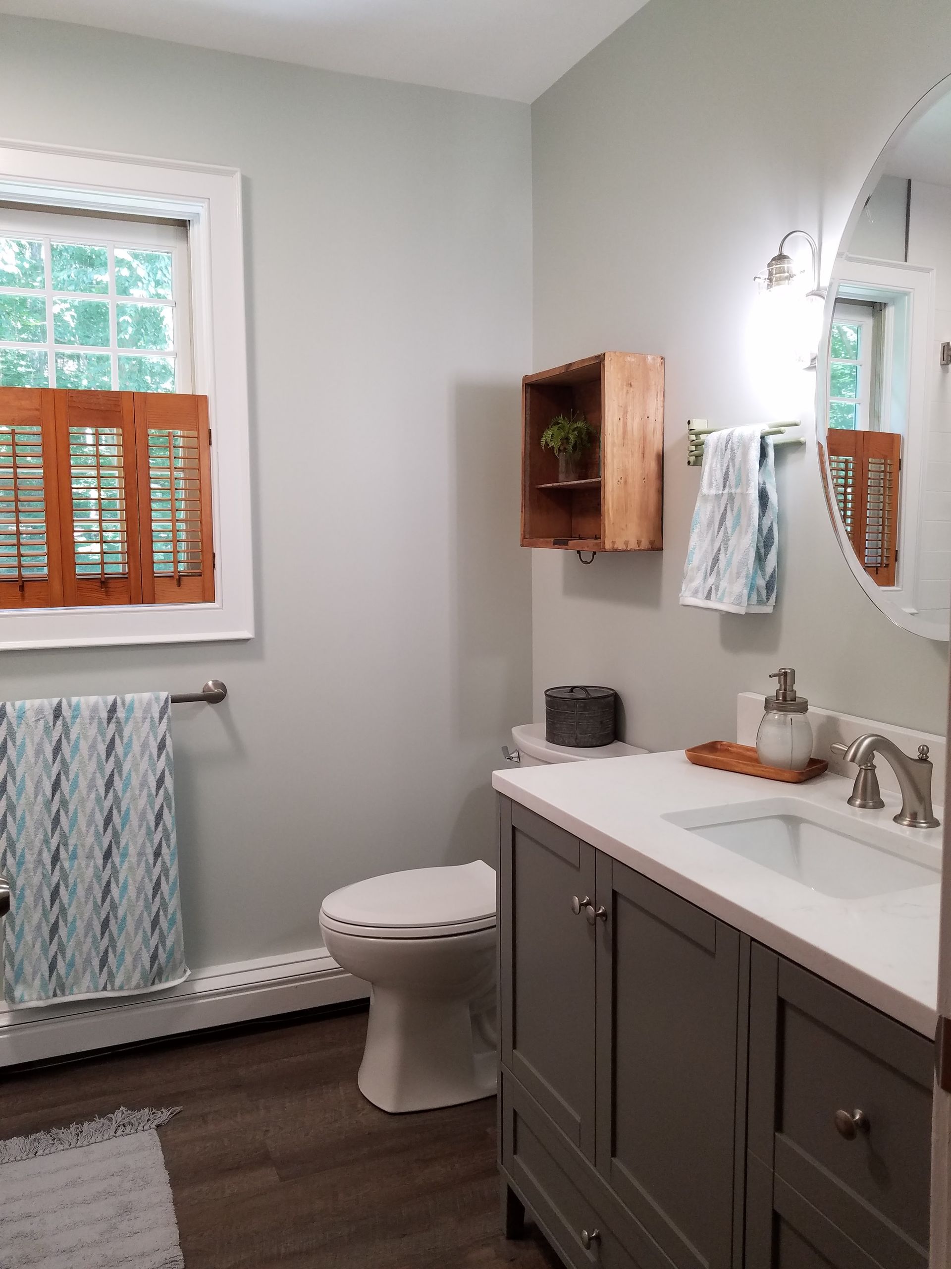 A bathroom with a toilet , sink , mirror and window.