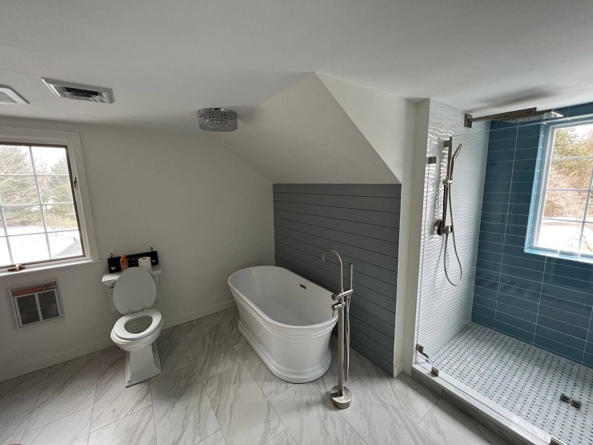 A bathroom with a tub , toilet , shower and window.
