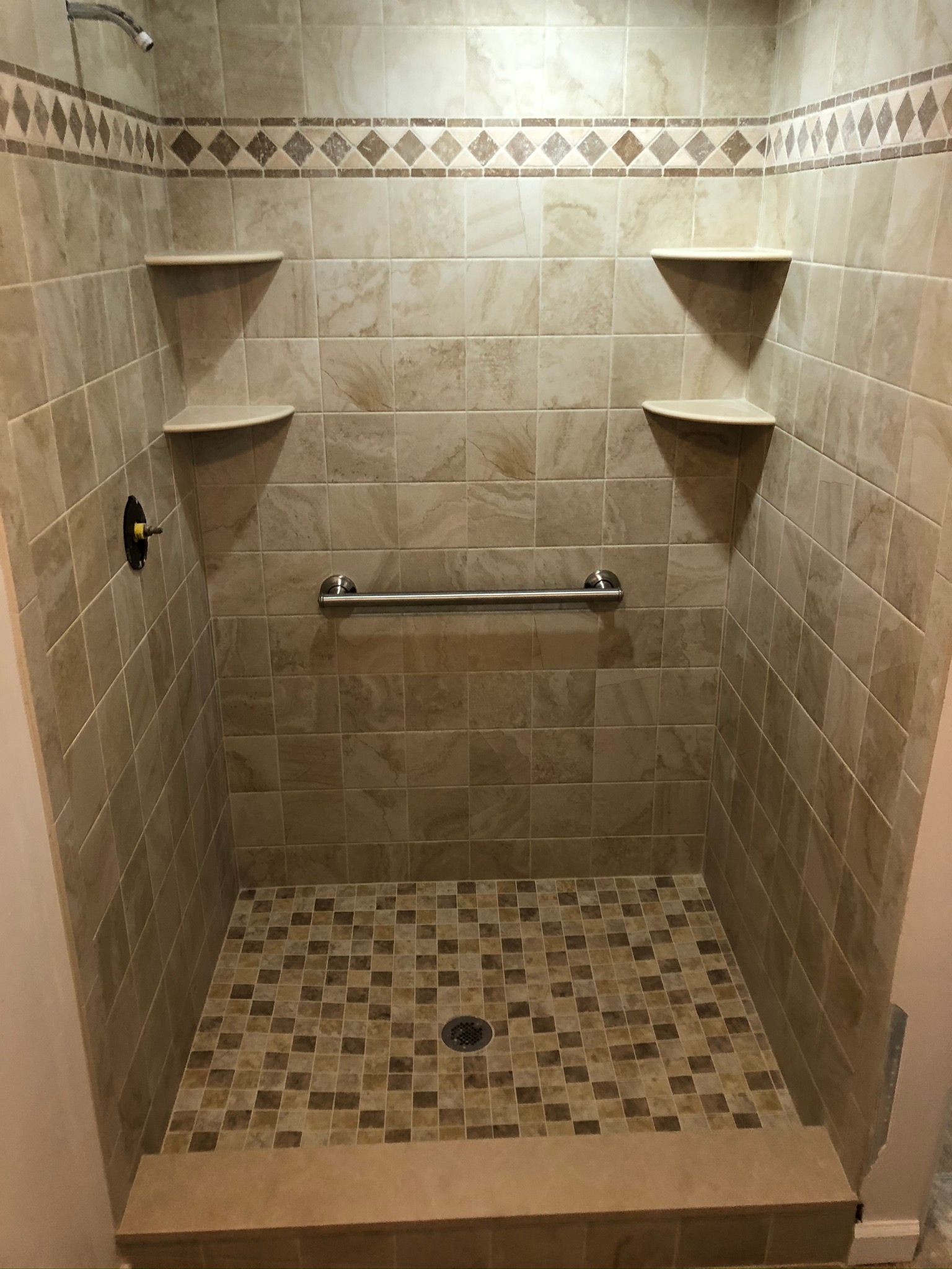 A walk in shower with a tiled floor and shelves.