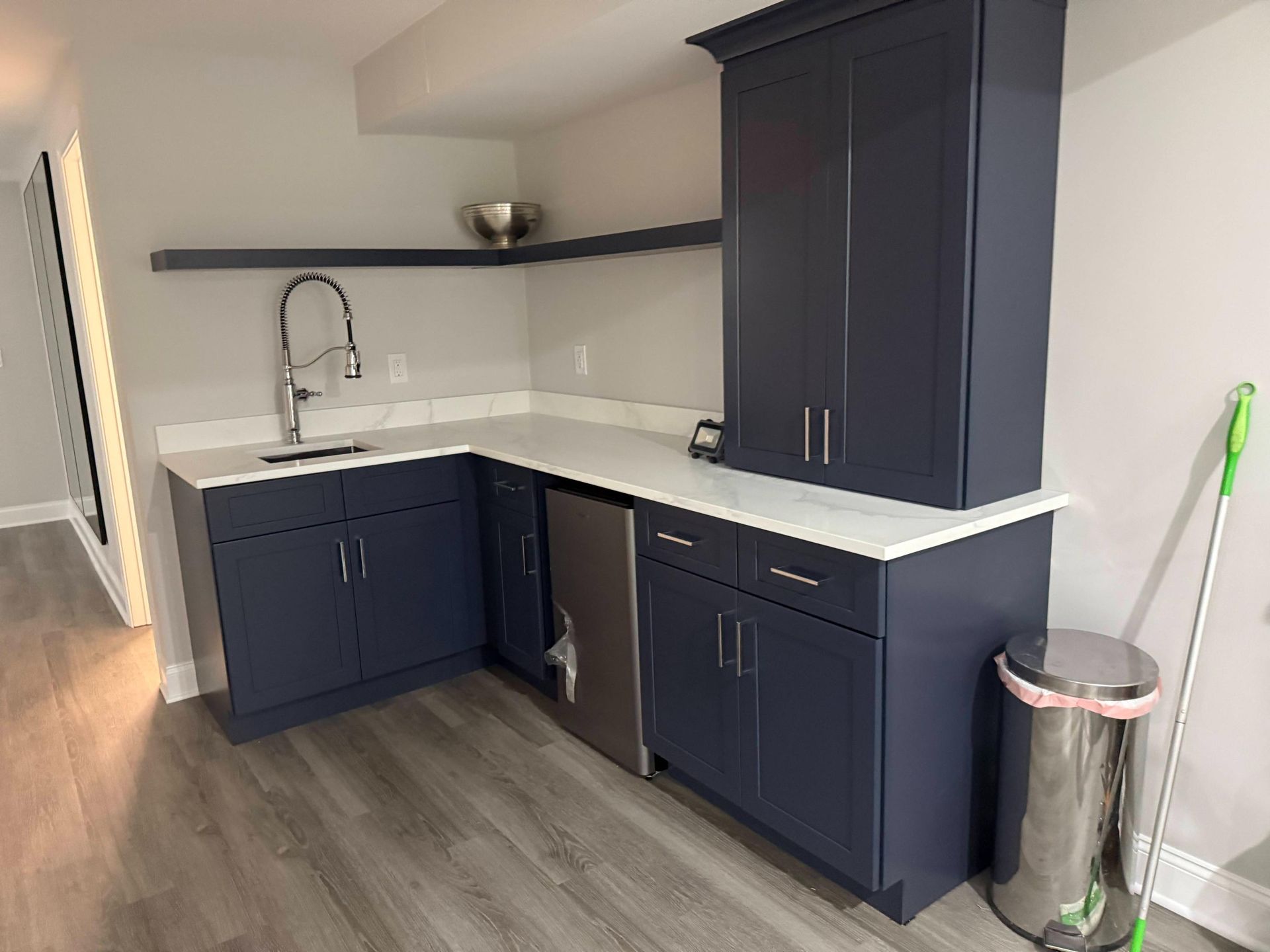 Modern kitchen corner with navy cabinets, white countertops, sink, and gray wood flooring.