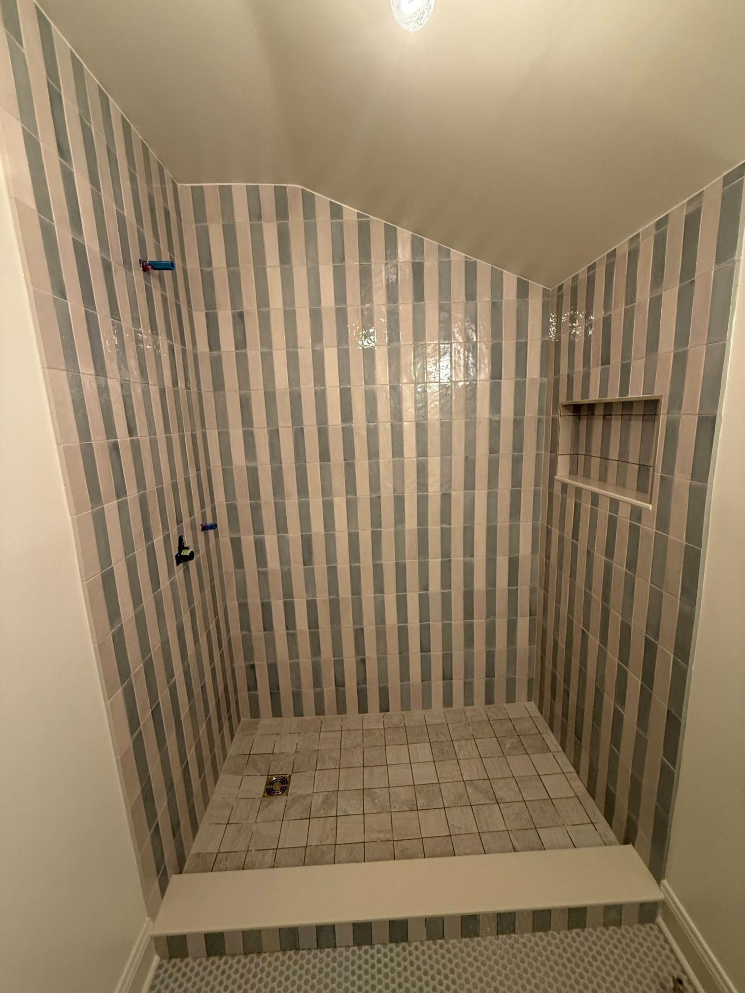 Empty tiled shower with striped walls, built-in shelf, and low step-up entry.