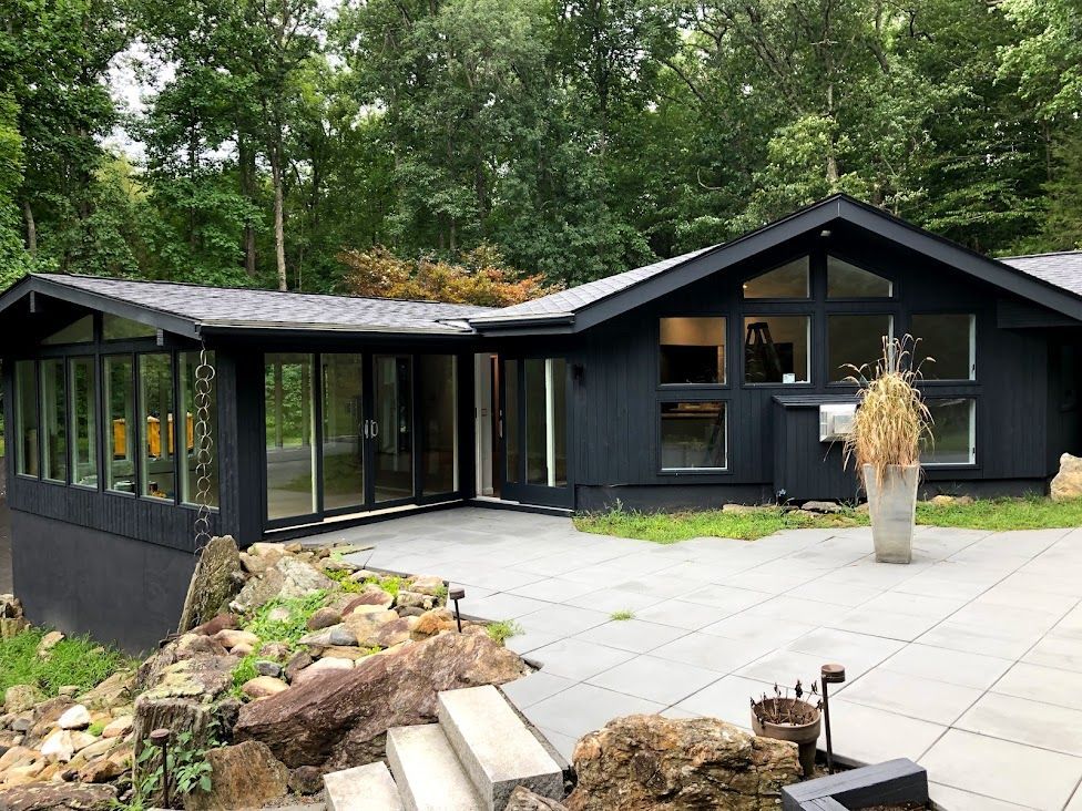 A black house with a lot of windows is surrounded by trees.