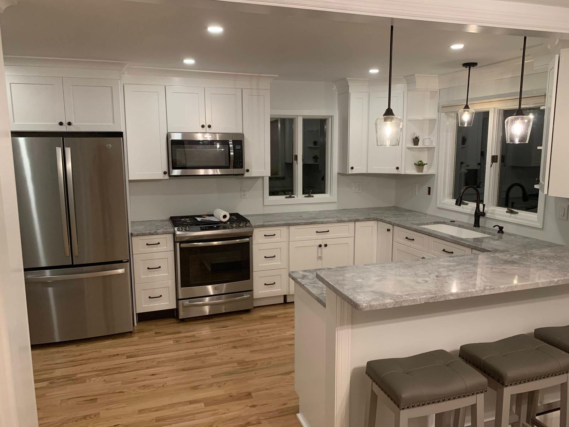 Bright modern kitchen with white cabinets, stainless appliances, marble countertops, and barstools