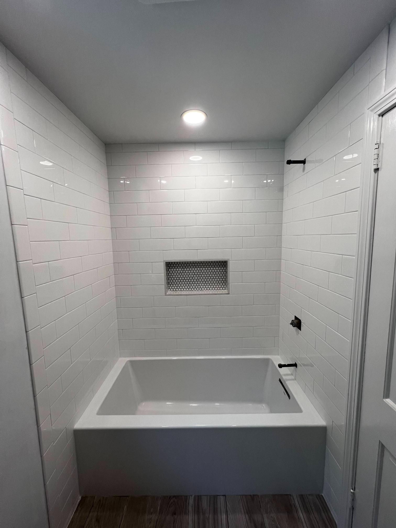 White tiled bathroom with a walk-in soaking tub and recessed wall niche.