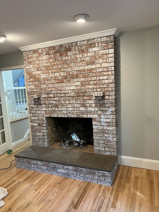 A living room with a brick fireplace and hardwood floors.