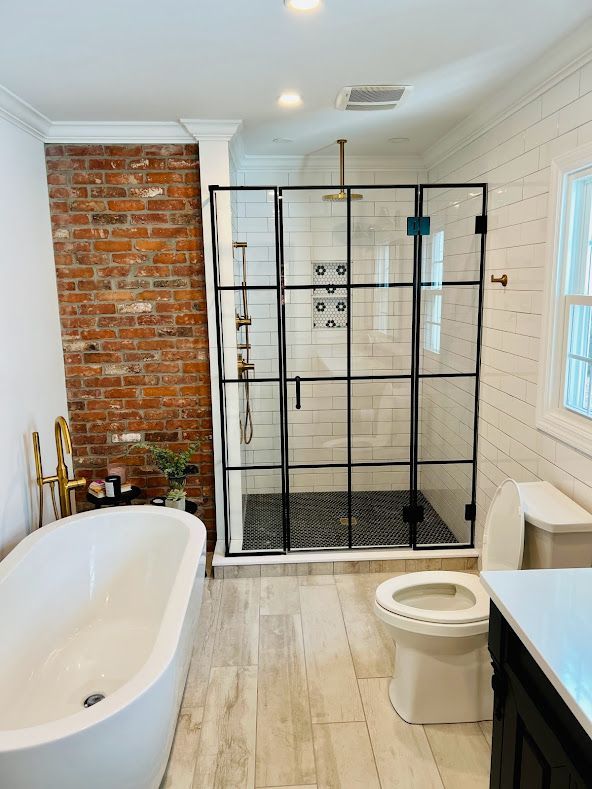 A bathroom with a tub , toilet , shower and brick wall.