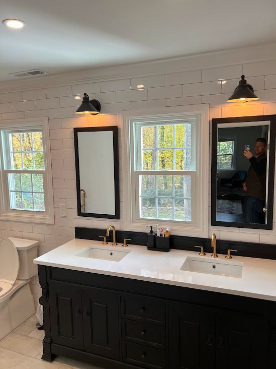A bathroom with two sinks , two mirrors and a toilet.