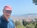 A man wearing a red hat and sunglasses stands in front of a city