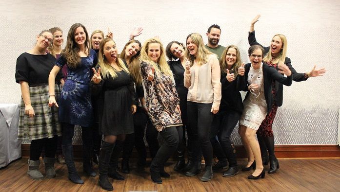 Eine Gruppe von Frauen posiert und lächelt gemeinsam in einem Innenraum; sie tragen dunkle und helle Outfits.