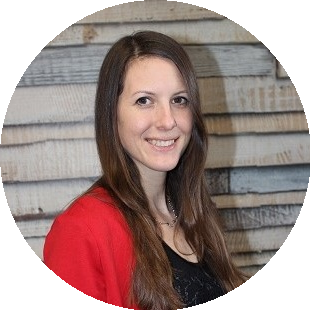 Porträt einer lächelnden Frau mit langen braunen Haaren, die eine rote Strickjacke trägt, vor einer Holzwand