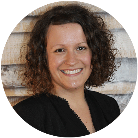 Lächelnde Frau mit lockigem, dunklem Haar und schwarzem Oberteil vor einer Steinmauer