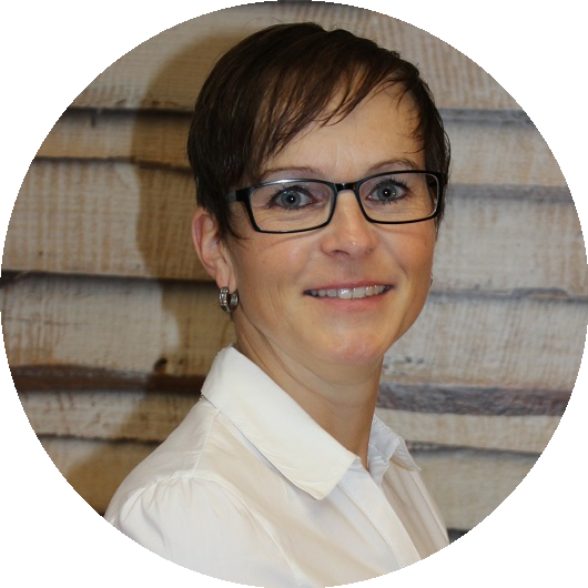 Lächelnde Person mit Brille und kurzen dunklen Haaren, die ein weißes Hemd trägt, vor einem strukturierten beigen Hintergrund