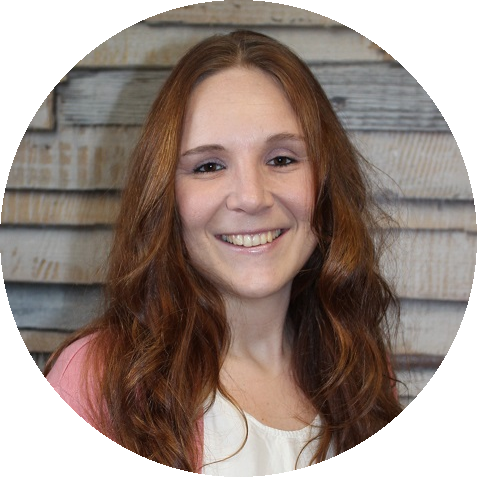 Lächelnde Frau mit langen, rötlichen Haaren in einem rosa Pullover vor rustikalem Holzhintergrund