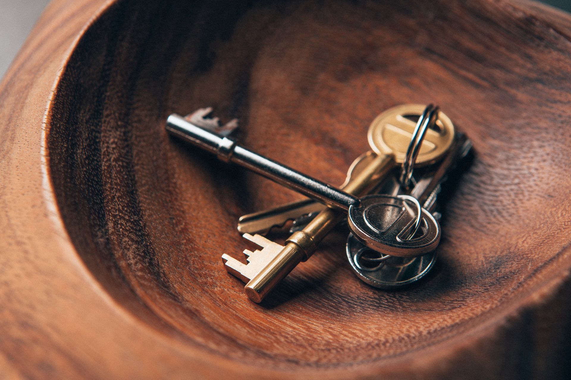 A bunch of keys are sitting on top of a wooden bowl.