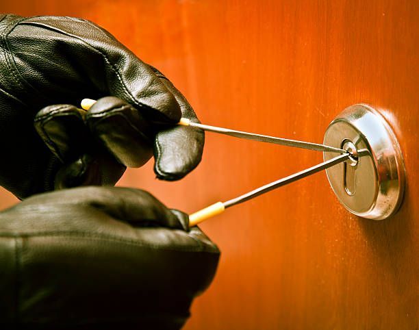 A person wearing black gloves is using a screwdriver to open a door lock