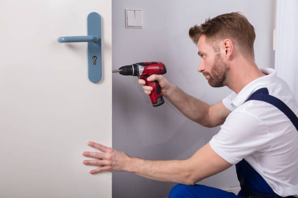 A man is using a drill to fix a door handle.