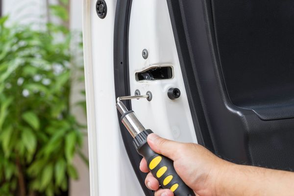 A person is using a screwdriver to fix a car door lock.