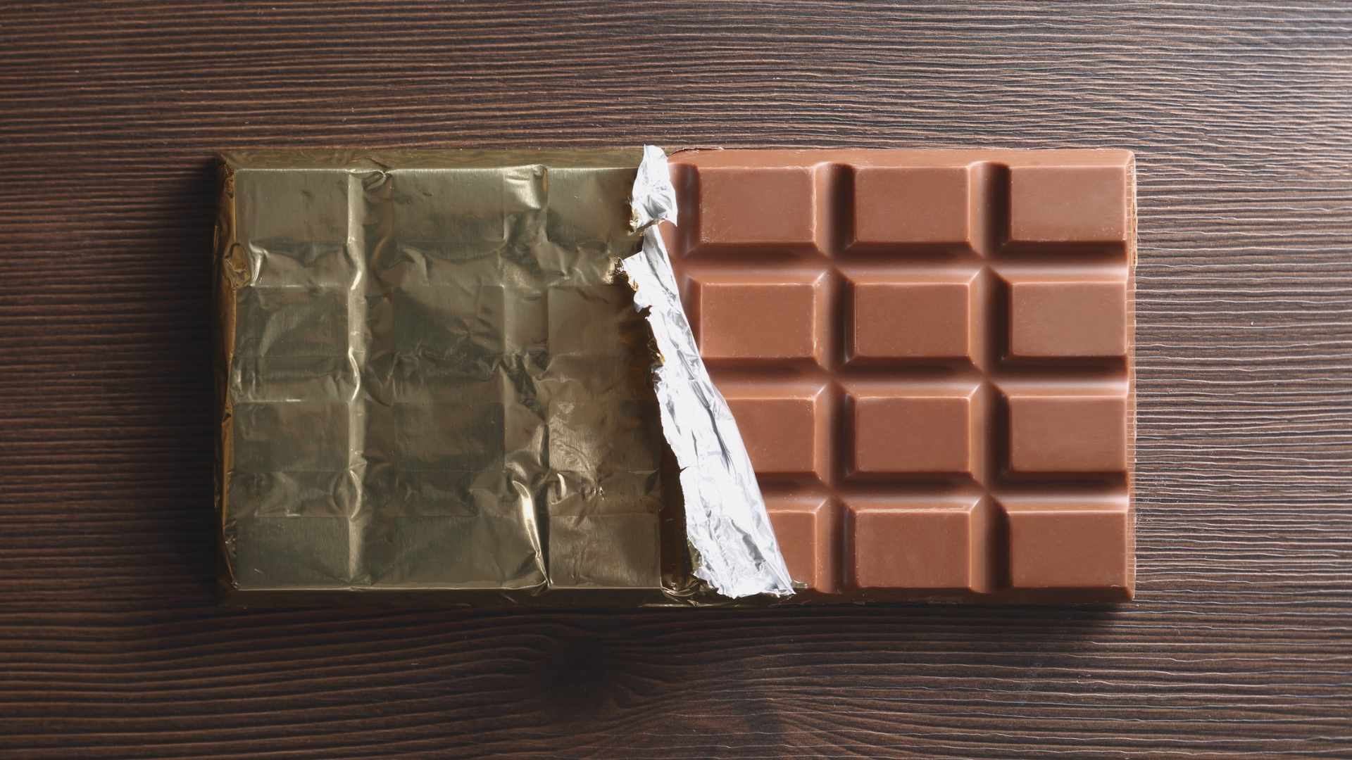 A chocolate bar is broken in half on a wooden table.
