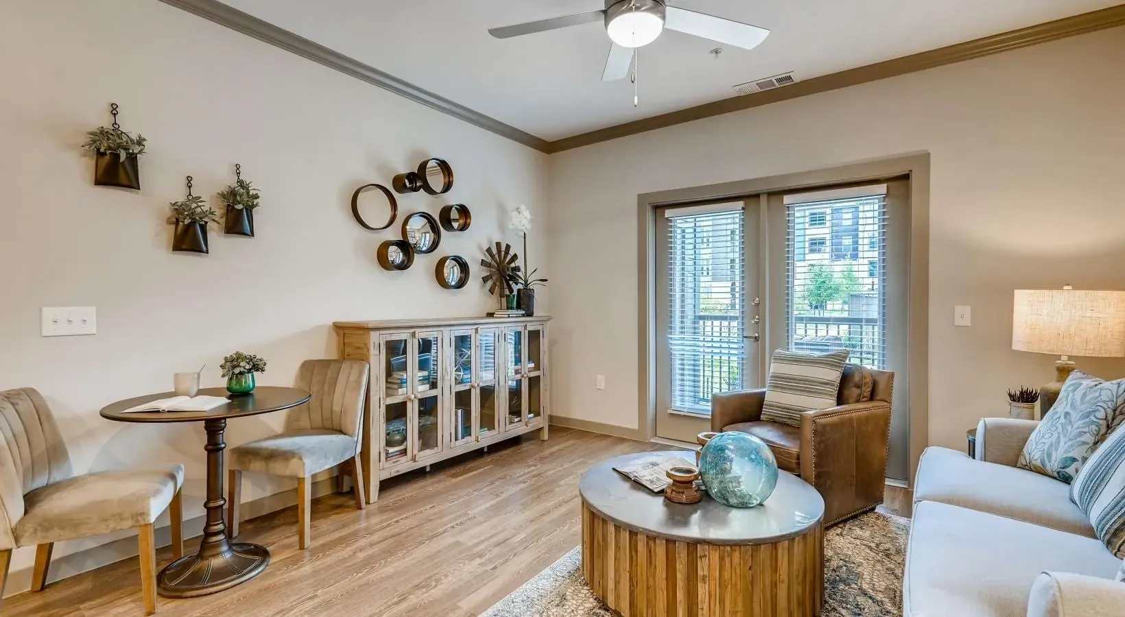 Living room of an apartment with beige seating, a wooden cabinet, wall decor, and a glass balcony door.