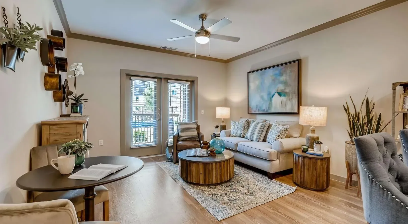 Living room with sofa, chairs, coffee table, rug, lamps, and wall art near balcony doors.