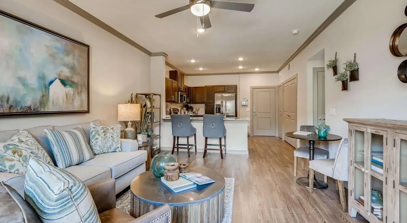 Open-concept living area with a gray sofa, decorative pillows, round coffee table, and a kitchen island with two bar stools.