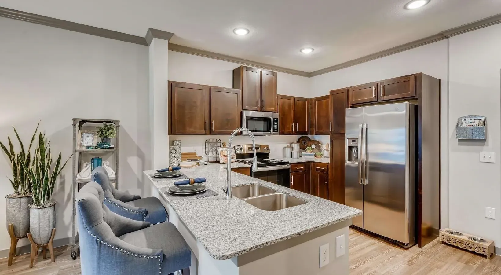 Modern apartment kitchen with granite island, stainless steel appliances, and dark wood cabinets.