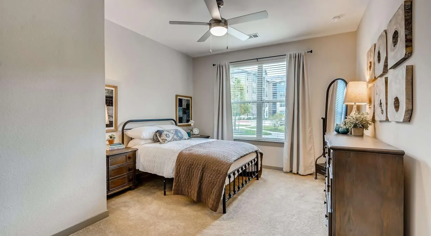 Bedroom in an apartment with a metal bed frame, nightstands, dresser, and a window.