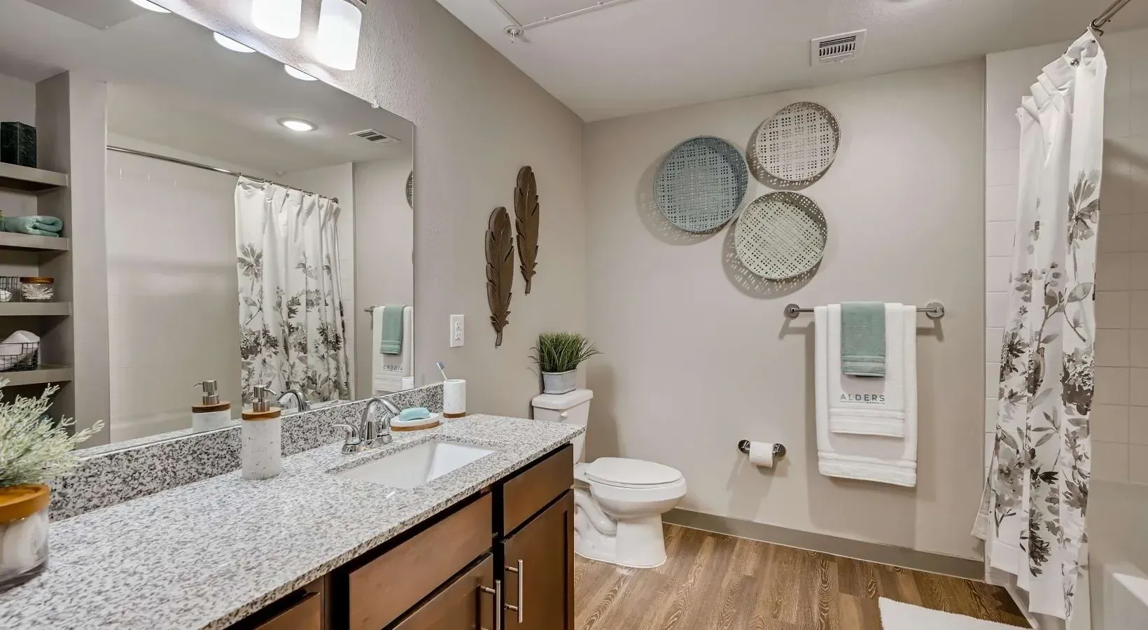 Bathroom interior with granite vanity, single sink, large mirror, towel rack, and floral shower curtain.