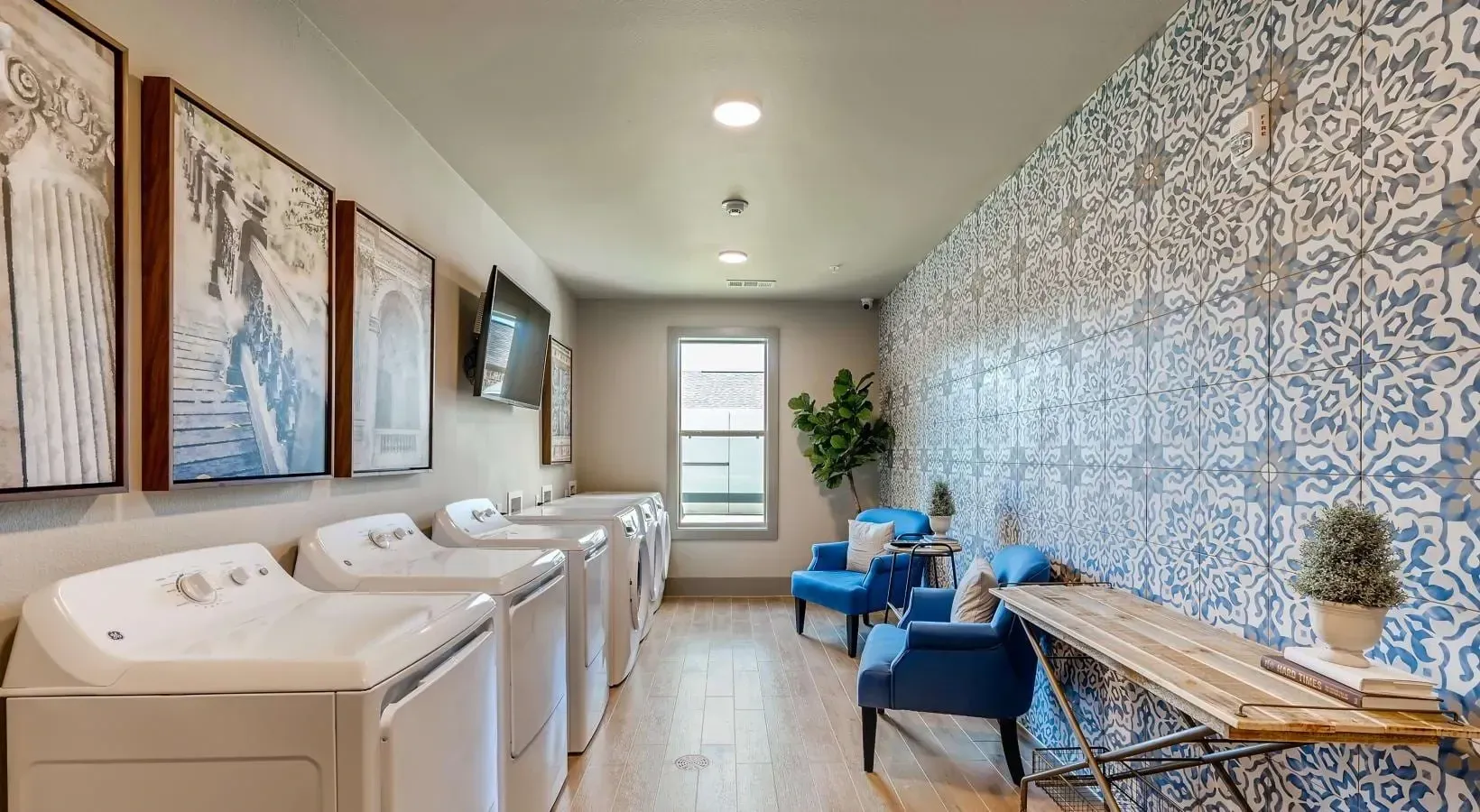 Laundry room with multiple front-loading washers along left, blue seating area, and a patterned blue tile wall on the right.