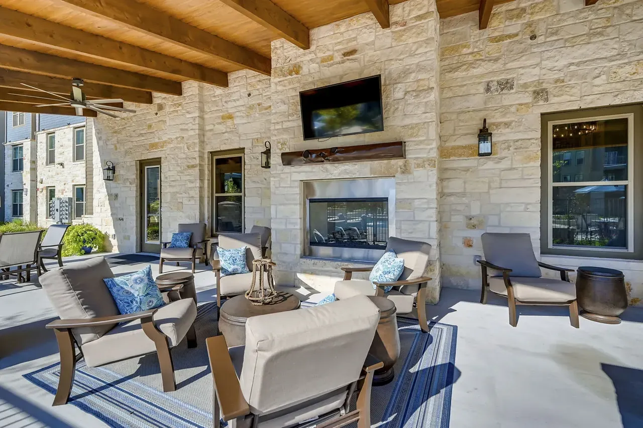 Outdoor covered lounge with stone fireplace, TV, and cushioned chairs.