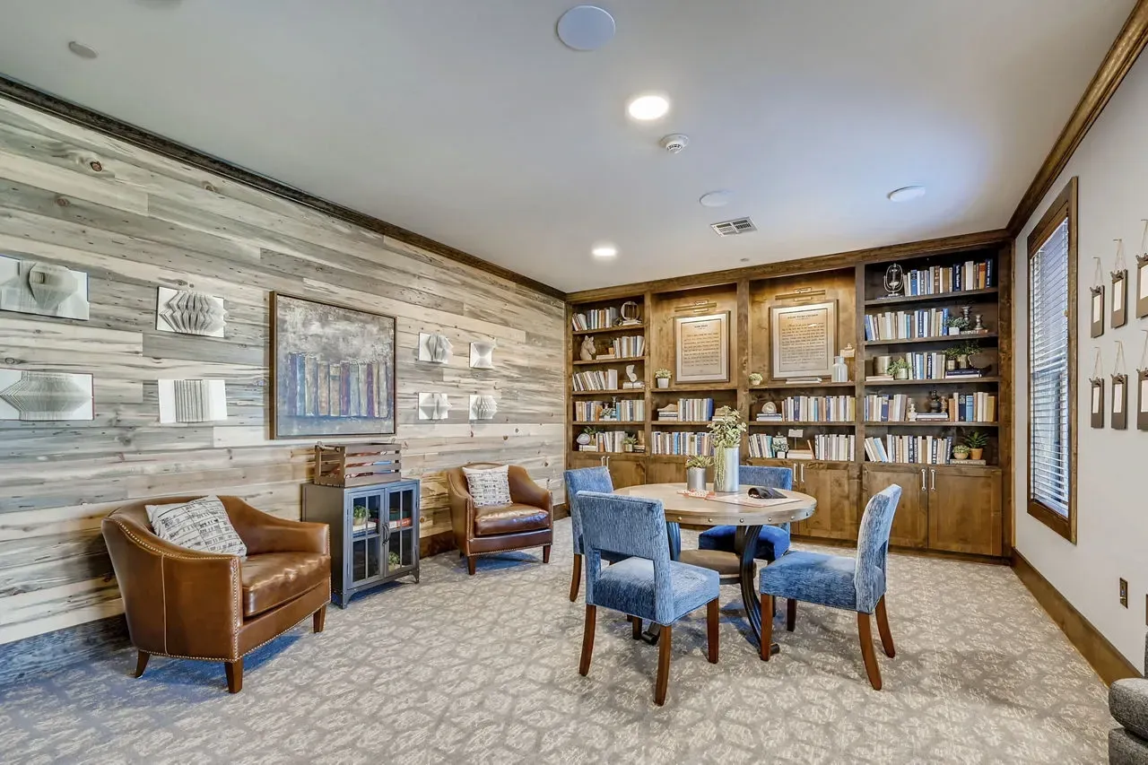 Interior community lounge with round table, blue chairs, and built-in bookshelves.